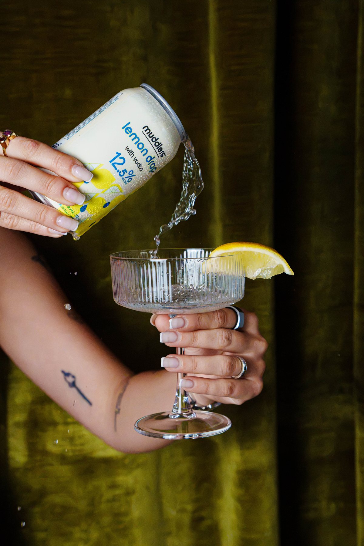 Muddlers Lemon Drop being poured from the can into a coupe with a lemon wedge