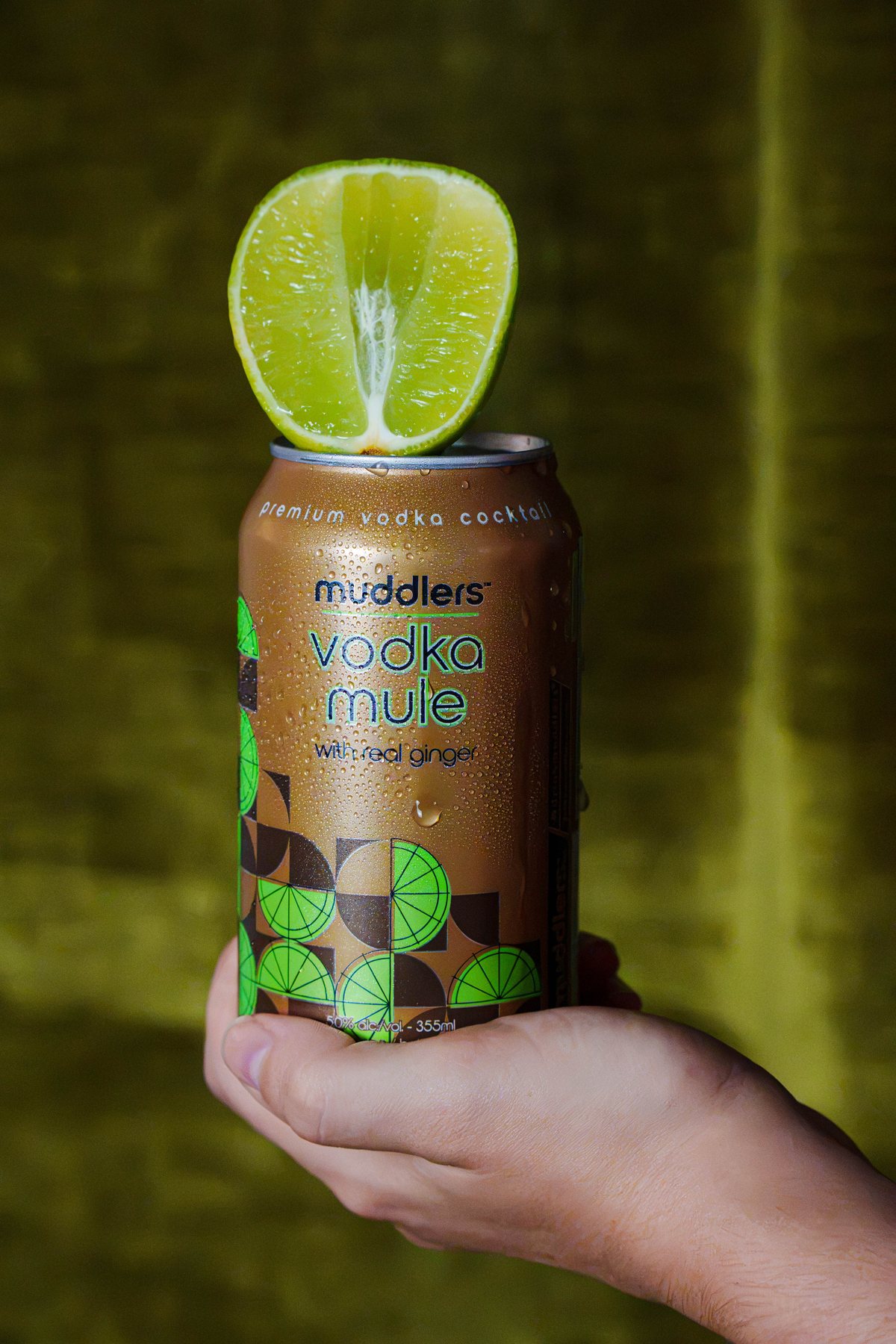 A hand holding up a can of Muddlers Vodka Mule topped with half a lime